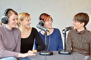 Vier junge Frauen sitzen am Tisch mit Mikrofonen und Kopfhörer.