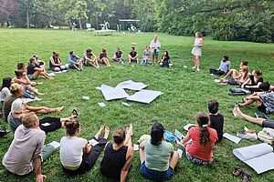 About 30 people sitting in a circle on a meadow. 