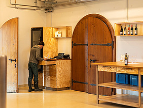 Raum mit einer Theke auf der Wein steht und Person im Hintergrund.