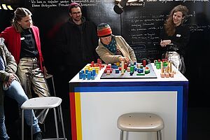 Vier Personen an einem Tisch, eine Person bewegt die Holzklötzchen darauf.