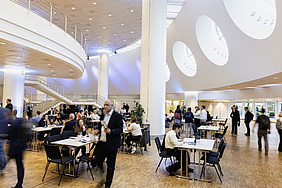 Large hall with people passing by and sitting at desks.