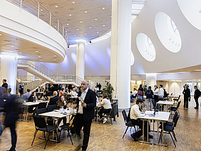 Large hall with people passing by and sitting at desks.