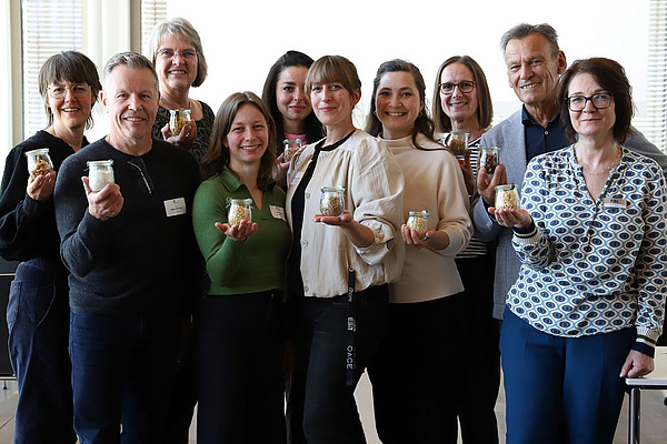 Zehn Personen präsentieren kleine Gläser mit verschiedenen Inhalten.