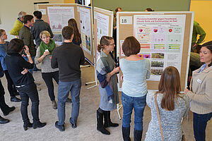 Several people are standing in a room with poster boards and discussing