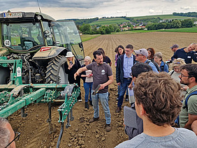 Ein Mann erklärt einer Gruppe von Menschen eine landwirtschaftliche Maschine.