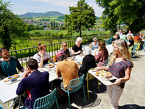 Menschen essen an einem langen Tisch auf einer Terrasse.
