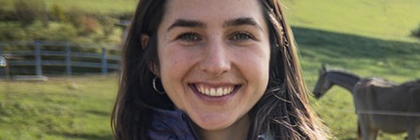 Eine Frau steht auf der Weide mit Kühen im Hintergrund.