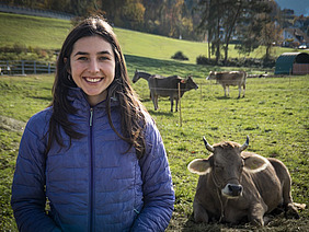 Eine Frau steht auf der Weide mit Kühen im Hintergrund.