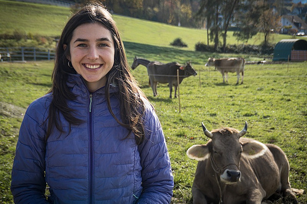 Eine Frau steht auf der Weide mit Kühen im Hintergrund.