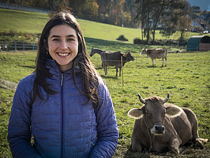 Eine Frau steht auf der Weide mit Kühen im Hintergrund.