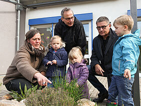 Kinder und Erwachsene ernten Schnittlauch  einer Kräuterspirale.