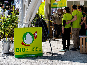 Die Knospe von Bio Suisse an einem Stand mit Menschen.