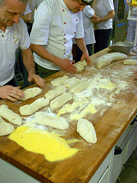 Teilnehmer eines Bäckerseminars bearbeiten Teiglinge.