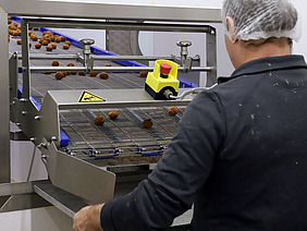 Mann mit einer Haube auf dem Kopf vor einer Produktionsmaschine.