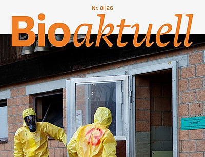 Titelseite Bioaktuell 8|26: Drei Menschen in Schutzanzügen und Atemmasken beim Eingang zu einem Stall.
