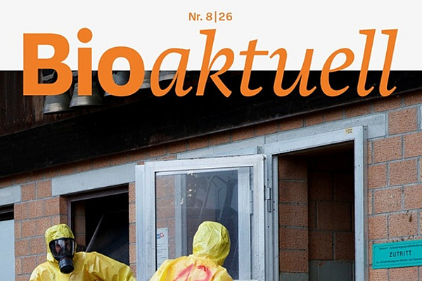 Titelseite Bioaktuell 8|26: Drei Menschen in Schutzanzügen und Atemmasken beim Eingang zu einem Stall.