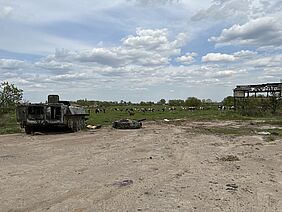 In the background a meadow with cows, in the foreground a destroyed tank and the scaffolding of a house.