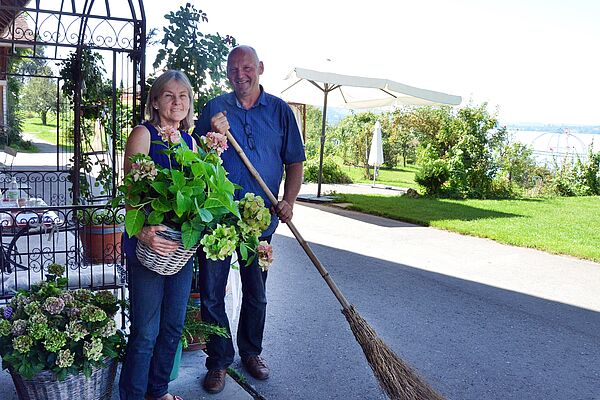 [Translate to Französisch:] Ein Mann und eine Frau stehen auf ihrem Hof, im Hintergrund sieht man den Zugersee.