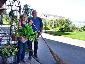 Ein Mann und eine Frau stehen auf ihrem Hof, im Hintergrund sieht man den Zugersee.