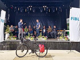 Mehrere Menschen auf einer Bühne, davor ein Fahrrad.