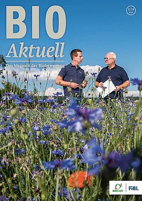 Titelseite Bioaktuell, zwei Männer im Gespräch auf einem Feld, im Vordergrund blaue Blumen.