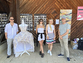 Vier Personen und eine Schaufensterpuppe mit Kleid posieren vor einer Wand mit Bildern.