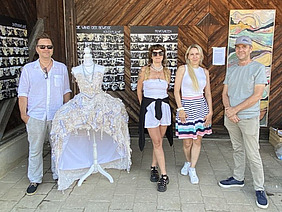Vier Personen und eine Schaufensterpuppe mit Kleid posieren vor einer Wand mit Bildern.