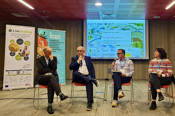 Four people sitting in front of a screen and banners.