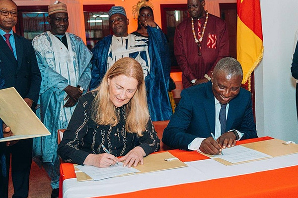 A woman and a man sitting on a desk, signing a document.