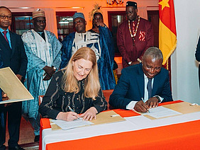 A woman and a man sitting on a desk, signing a document.