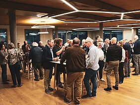 Besuchende stehen an Stehtischen und nehmen ein Apéro zu sich und unterhalten sich.
