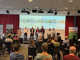 Menschen sitzen in einem Raum und hören einem Vortrag zu.