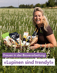 Eine Frau um die 30 kniet in einem reifen Feld und hält einen Korb voller schön angerichteter Produkte. Die Frau ist blond und strahlt über das ganze Gesicht. Im Text steht "Lupinen sind trendy"