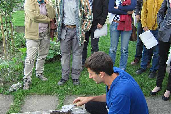 Mann zeigt Teilnehmern Erde aus einem Blumenkasten