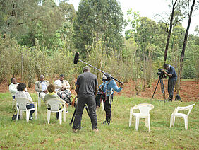 Three people filming a group of people on chairs