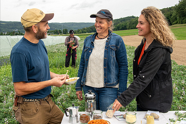 A man and two women at a table with various products in a field.
