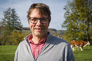 A man on a meadow with a cow in the background.