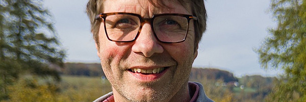 Un homme dans un pré avec une vache en arrière-plan.