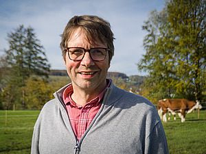 Un homme dans un pré avec une vache en arrière-plan.