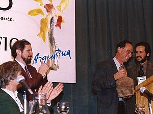 Four men on a stage, two of them applauding. 