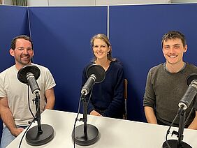 Die Gäst*innen des Podcasts sitzen hinter den Mikrofonen