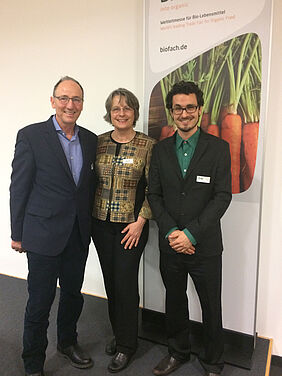 Portrait photo of three people in front of a Biofach banner.