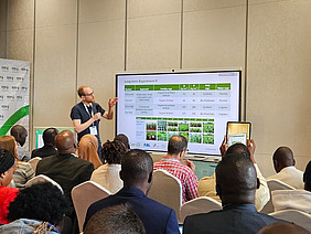 A man explaining a table on a screen with a group of people sitting and watching him.