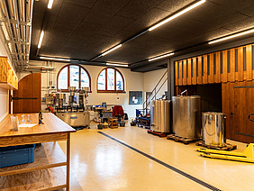 Raum mit Theke, Metallfässern und weiteren Gerätschaften. 