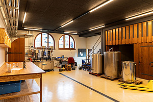 Raum mit Theke, Metallfässern und weiteren Gerätschaften. 