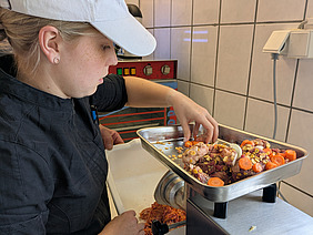 Frau dreht Gemüse und Fleisch durch einen Fleischwolf.