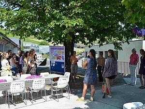 Group of people standing under a tree around a poster.