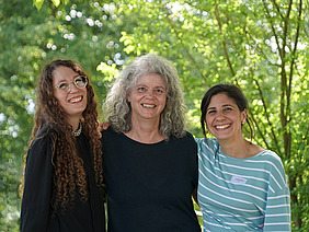 Three women in front of a leavy background.