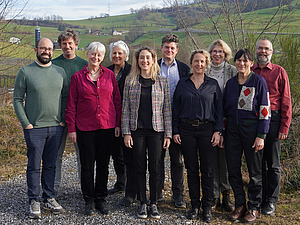 Eine Gruppe von Menschen mit grünem Hügel im Hintergrund.