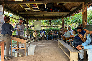 A group of people sitting under a hut. Two people demonstrating an experiment. 